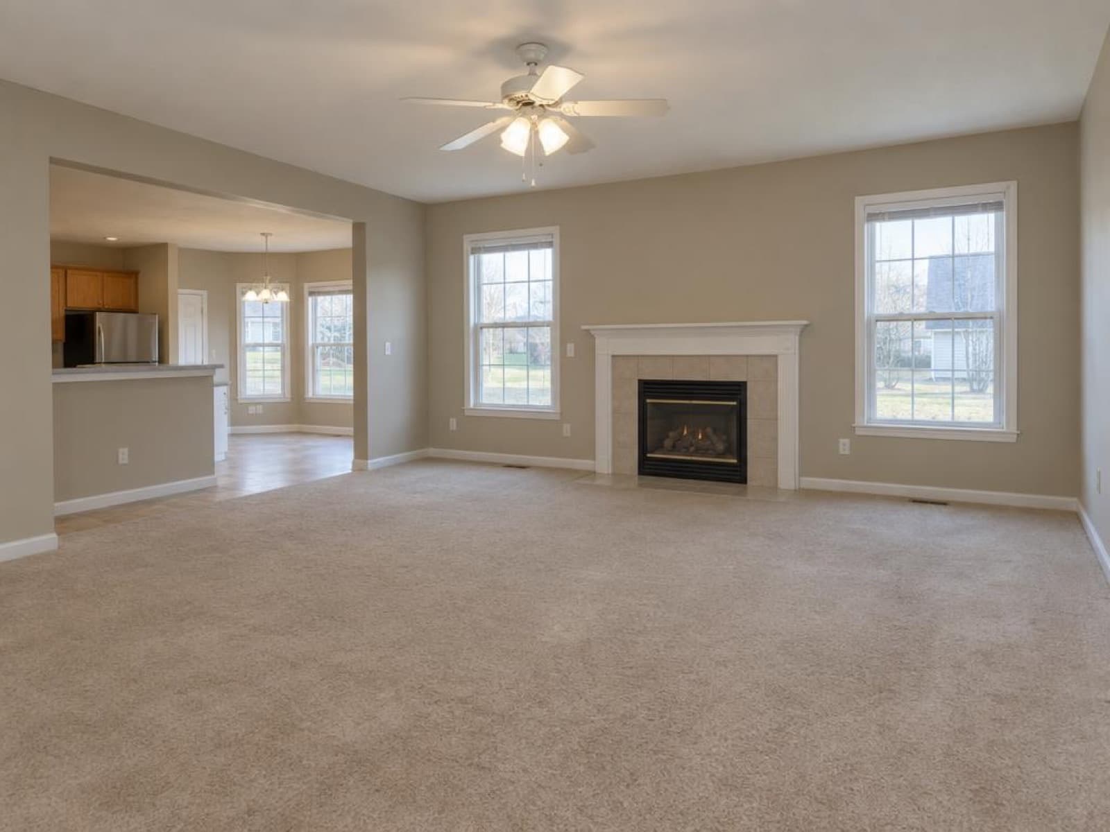 Empty suburban living room with beige carpet, a ceiling fan and a gas fireplace