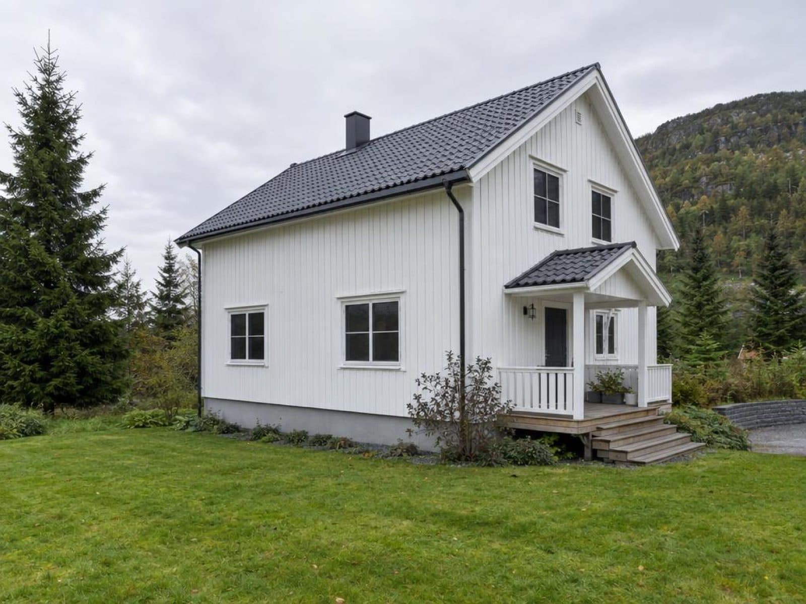 Hvitt norsk trehus med veranda fotografert på dagtid