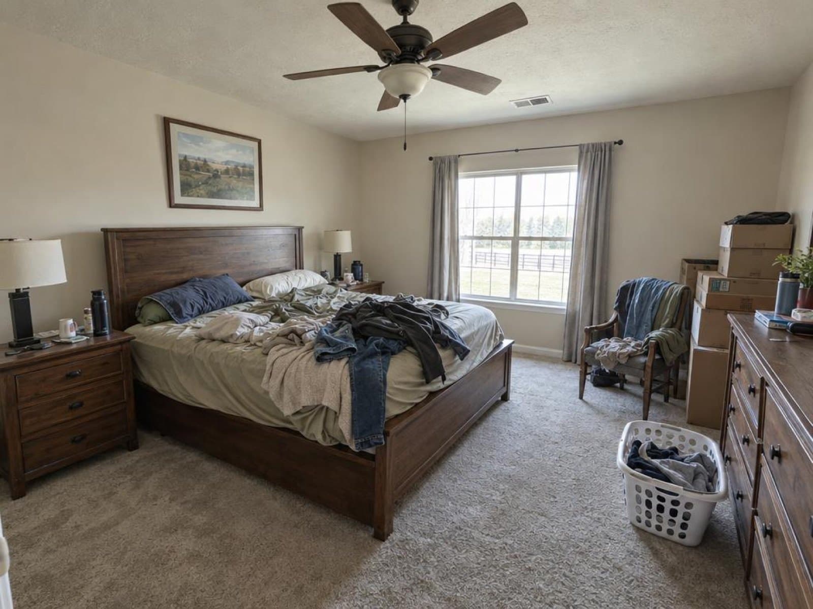 Bedroom photographed on a phone with an unmade bed, piled clothes, boxes and a laundry basket