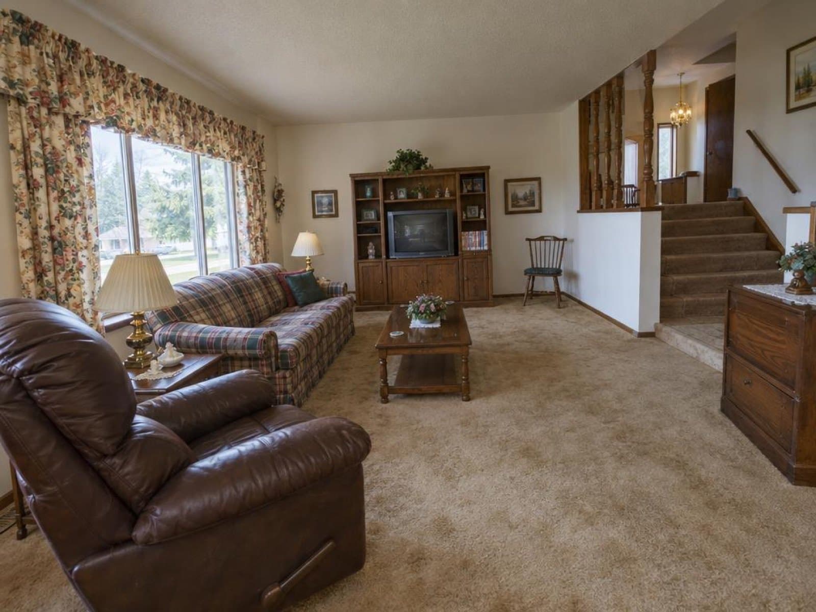 Dated living room with a leather recliner, plaid sofa and floral curtains