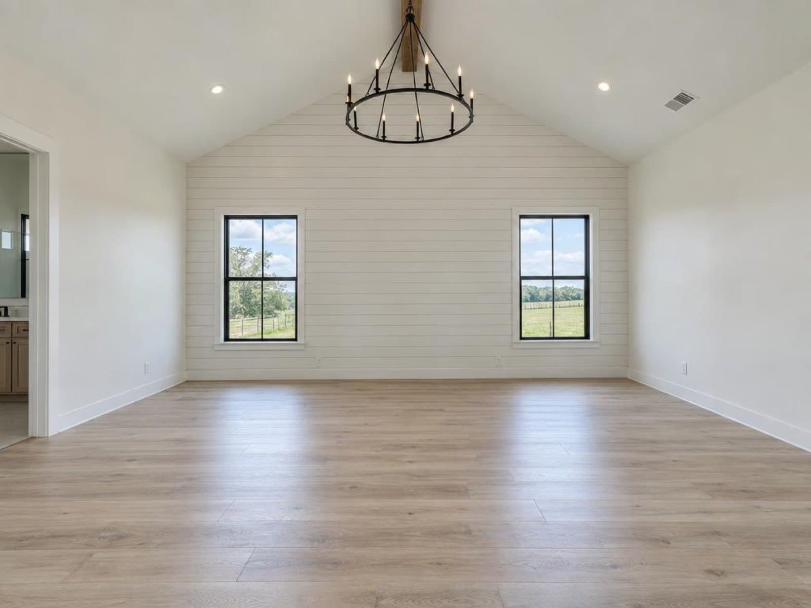 Empty primary bedroom with shiplap wall and vaulted ceiling