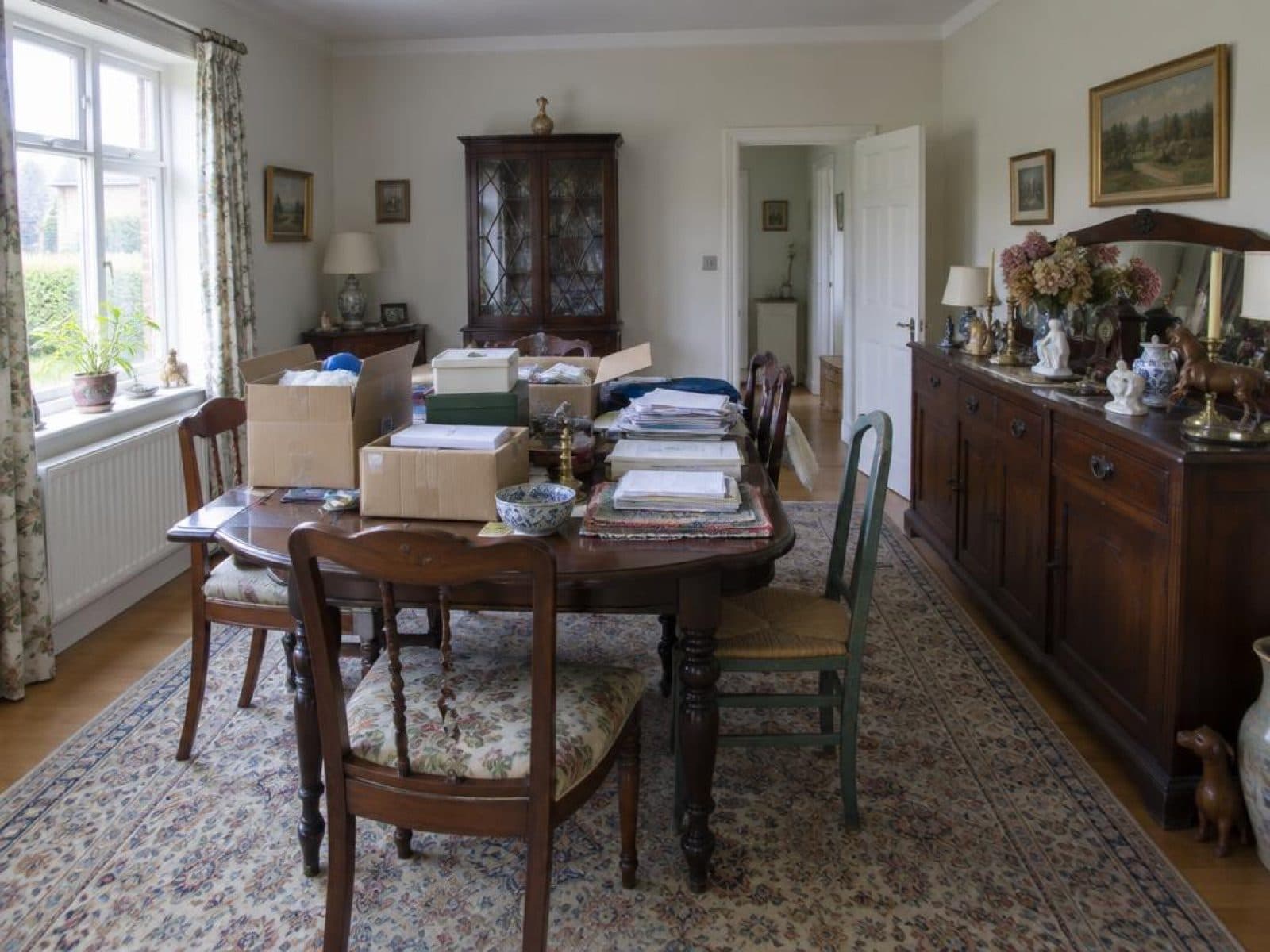 Cluttered dining room with boxes on the table and mismatched chairs